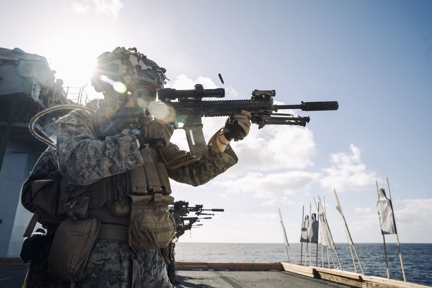 A Marine firing a rifle on a ship's deck toward targets