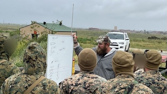An instructor at a whiteboard teaching wind calls to a class of snipers; faces blurred